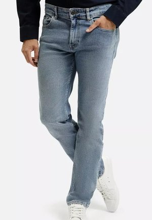 Jasnoniebieskie dżinsy o klasycznym kroju, z pięcioma kieszeniami i zapięciem na guzik. Noszone z ciemną bluzką i białymi trampkami, ukazując detale w strukturze materiału.