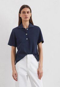 Marineblaues Baumwoll-Polohemd mit kurzen Ärmeln, flachem Kragen und drei Knöpfen. Hat eine lockere Passform und Seitenschlitze für Bewegungsfreiheit.