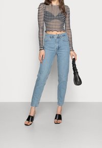 Blusa de manga larga de sheer a rayas en blanco y negro, jeans de cintura alta en azul claro, sandalias negras de tacón cuadrado y un bolso negro.