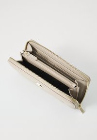 Portafoglio in pelle beige con zip dorata, scomparti interni e fessure per carte. Dispone di una tasca con zip e una superficie liscia.