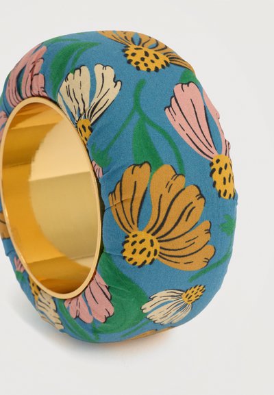 Πλατιά χρυσή βραχιόλισε βραχιόλι τυλιγμένη σε ύφασμα με μπλε φόντο και λουλουδάτο μοτίβο σε κίτρινες, ροζ, λευκές και πράσινες αποχρώσεις.