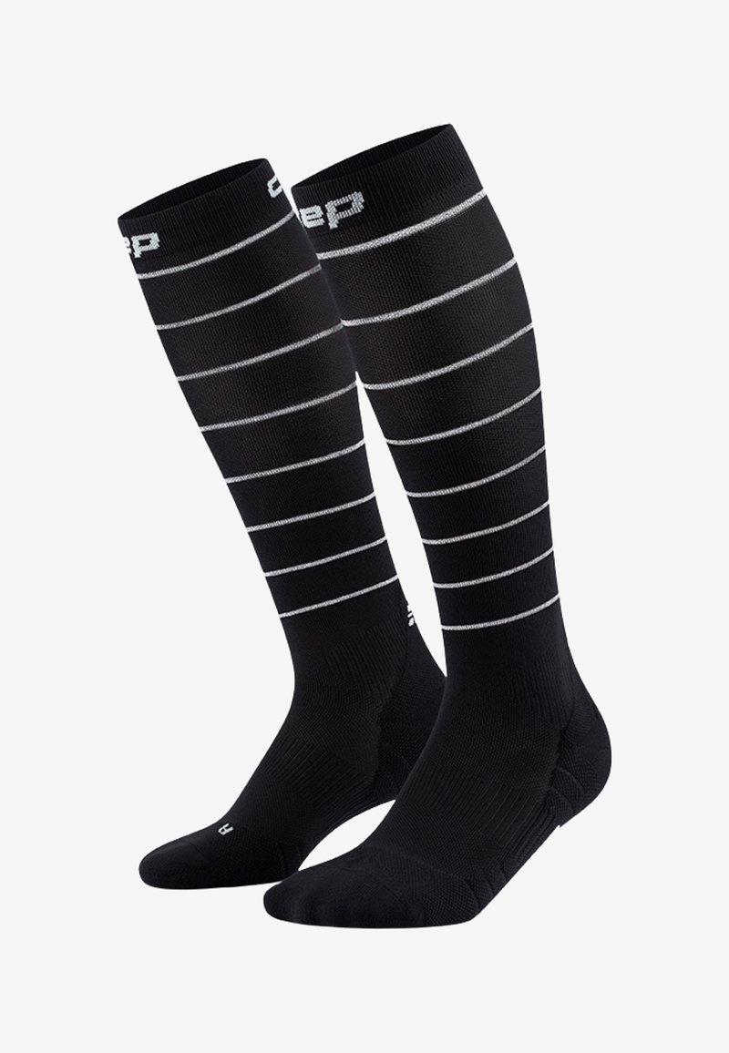Schwarze Kompressionssocken mit weißen horizontalen Streifen. Hergestellt aus elastischem Material, mit einer strukturierten Oberfläche und verstärktem Zehen- und Fersenbereich.