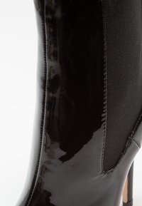 Stivale alla caviglia in pelle verniciata nera con un pannello in tessuto testurizzato, finitura liscia, punta appuntita e tacco a stiletto.