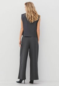 Top negru fără mâneci cu un design structurat, asociat cu pantaloni negri cu picioare largi și pantofi cu toc ascuțit negri. Textură de țesătură netedă.