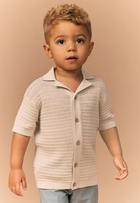 Lysebeige strikket cardigan med korte ærmer og krave, udstyret med knaplukning og et tekstureret mønster.