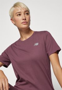 T-shirt κοντομάνικο, σε απόχρωση δαμάσκηνου, φτιαγμένο από μαλακό ύφασμα, που διαθέτει ένα μικρό ασημένιο λογότυπο New Balance στην αριστερή πλευρά του στήθους.