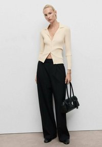 Top button-up a coste di colore crema con colletto, abbinato a pantaloni neri larghi e una piccola borsa nera. Tessuto morbido e design semplice.