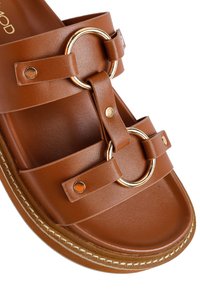 Sandalo in finta pelle marrone con hardware circolare dorato, design a doppia cinghia e cuciture crema sulla suola. Soletta testurizzata.