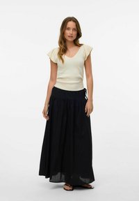Rebrasta kremna bluza s kratkimi letečimi rokavi, v kombinaciji z ohlapno črno maksi krilo s pasom na vrvico. Izgled dopolnjujejo ravni sandali.