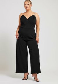 Schwarzer Jumpsuit mit weitem Bein, V-Ausschnitt und dünnen, verzierten Trägern. Hergestellt aus einem glatten, elastischen Stoff für Komfort und Passform.