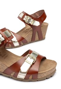 Bruine leren wedge-sandalen met metallic zilveren accenten. Kurkenzool, verstelbare bandjes, open teenontwerp en een getextureerde voetbed.