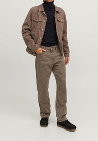 Brun denimjacka med silverknappar, bärs över en svart polotröja; kombineras med beige byxor och svarta mockaskor med gummisula.