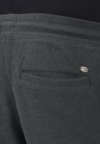 Gray denim pants featuring a rear pocket with a stitched opening and a small metal logo accent. The texture is ribbed and sturdy.
