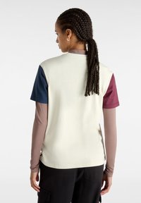 Top de manga corta con bloques de color que presenta un cuerpo beige, mangas en color marino y burdeos, y una camiseta interior marrón. Textura suave y ajuste relajado.