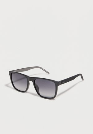 Black rectangular sunglasses with textured arms and gradient dark lenses, resting on a white surface.