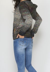 Multikleurige gebreide hoodie met een gestructureerd patroon, zwarte boorden en zakopeningen, gecombineerd met strakke blauwe jeans.