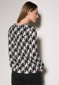 Pitkähihaista paitaa musta, valkoinen ja harmaa houndstooth-kuvio. Pehmeä kangas, rento malli, jossa on takana poimutus lisäyksinä.
