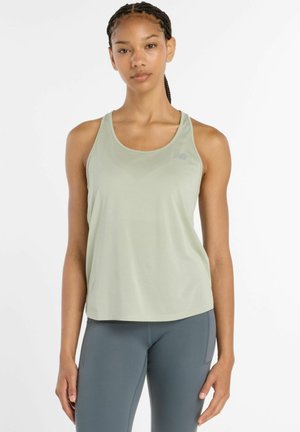 Ung kvinde med fletninger iført en lysegrøn ærmeløs sportstop og grå leggings med høj talje, stående mod en hvid baggrund.