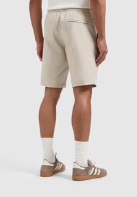 Beige shorts met een koord in de taille, een achterzak en een relaxte pasvorm, gedragen met bruine sneakers en witte sokken. Glad stoftextuur.
