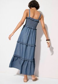 Denim maxi obleka z tankimi naramnicami, nabranim bodicem in volanastimi plastmi. Enotna modra barva, tekoča silhueta in dolžina do kolen.