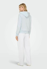 Jasnoniebieska bluza z kapturem z miękkiego materiału z kieszenią kangurką i sznurkiem, zestawiona z luźnymi szarymi spodniami dresowymi.