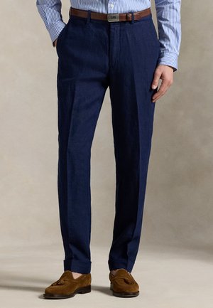 Παντελόνι από ναυτικό λινό με ίσια κοπή, διακοσμημένο με ραφές για πιέτα, τελειώματα με μανσέτες και καφέ δερμάτινη ζώνη. Συνδυασμένο με καφέ σουέντ μοκασίνια.