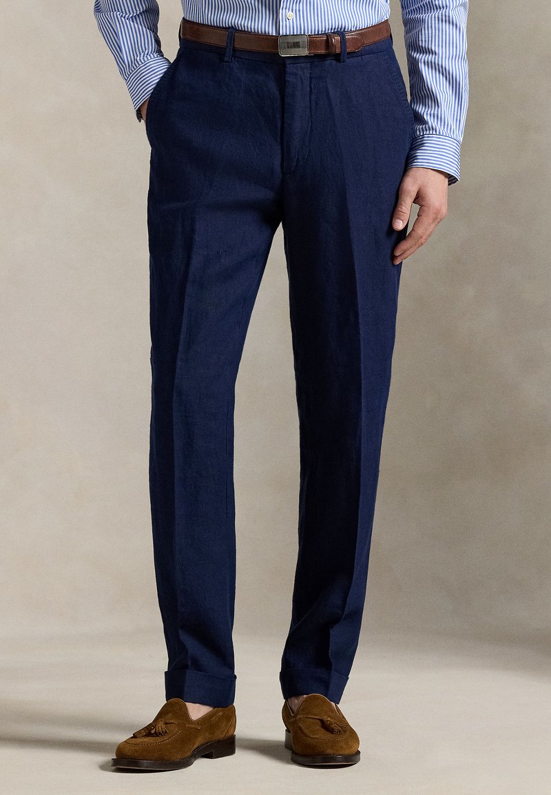 Marineblå linbukser med rette ben, pregesømmer, oppbrettede kanter og et brunt belte i skinn. Stylet med brune semskede loafers.