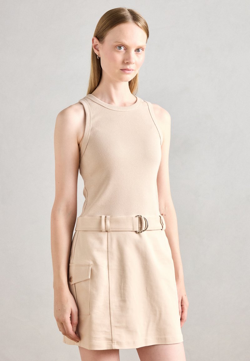 Débardeur côtelé beige associé �à une mini-jupe beige clair avec ceinture et poche latérale. Texture lisse et lignes épurées.