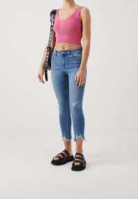 Růžový pletený crop top s výstřihem do V, modré roztrhané úzké džíny s třepenými okraji a černé sandály na remínky. Nastavitelný černý popruh tašky.