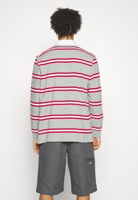 Graues Langarm-Polohemd mit roten horizontalen Streifen und einem weißen Kragen. Kombiniert mit grauen Shorts, die eine entspannte Passform und einen lässigen Stil zeigen.