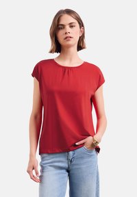 Haut rouge à manches courtes avec un col rond et des d�étails froncés. Assorti à un jean bleu clair. Tissu lisse et léger.