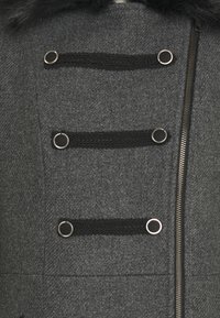 Abrigo de lana gris con cierre de cremallera y tres correas trenzadas negras con detalles plateados. El cuello está adornado con un suave ribete de piel que añade detalle.