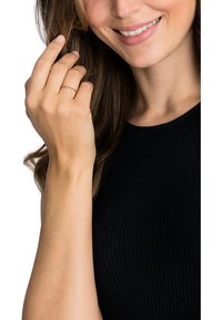 Guldvriden ring bärs på en hand med naturlackade naglar; modell som bär en svart ribbad topp, ler och har långt hår.