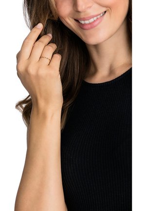 Gold twisted band ring worn on a hand with natural nail polish; model wearing a black ribbed top, smiling, with long hair.