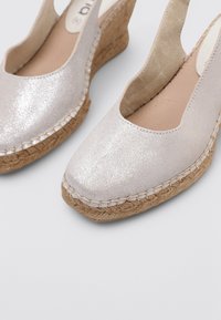 Alpargatas de cuña con un upper metálico plateado claro, que cuentan con una suela de yute y detalles de costura a lo largo del borde. Con lados abiertos para ventilación.