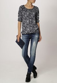 Top floral azul marino con mangas tres cuartos y cuello redondo, combinado con jeans skinny azules desgastados y botines negros. Clutch en mano.