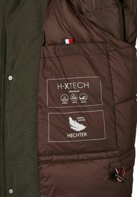 Binnenkant van de bruin geïsoleerde jas met H-XTECH-label, met iconen voor waterdicht en ademend. Inclusief details van dons en veren, ontwerpelementen.