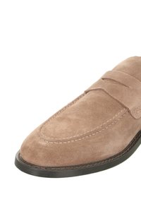 Beige Wildlederslipper mit runder Spitze, genähten Details und einer flachen schwarzen Gummisohle mit minimalen Akzenten.