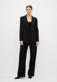 Zwart gestreept pak met een gestructureerde blazer met pieklapels en wijde broeken. Gladde stof met een getailleerde pasvorm.
