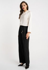 Biały top z długim rękawem i golfem, zestawiony z czarnymi szerokimi spodniami z subtelnym wzorem i sznurkiem w pasie. Czarne spiczaste buty.