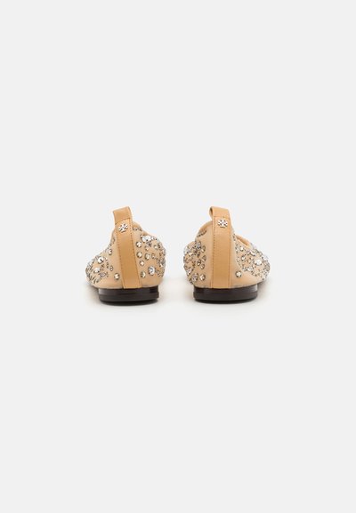 Chaussures en cuir beige au design incurvé, embellies de strass de différentes tailles, avec un petit talon et une languette à l'arrière.