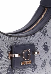 Borsa a spalla in tessuto blu marina con un motivo testurizzato, caratterizzata da un logo "G" in tono oro e dettagli hardware, un bordo in pelle liscia e chiusura con zip.