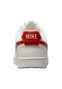 Sneaker bianca realizzata in materiali in pelle e mesh. Caratterizzata da una striscia arancione e da un tassello sul tallone esagonale con la parola "NIKE" in rilievo.