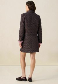 Veste à motif marine avec un design court et des accents de poignets roses, associée à une jupe courte assortie. Présente des éléments en or et un tissu texturé.