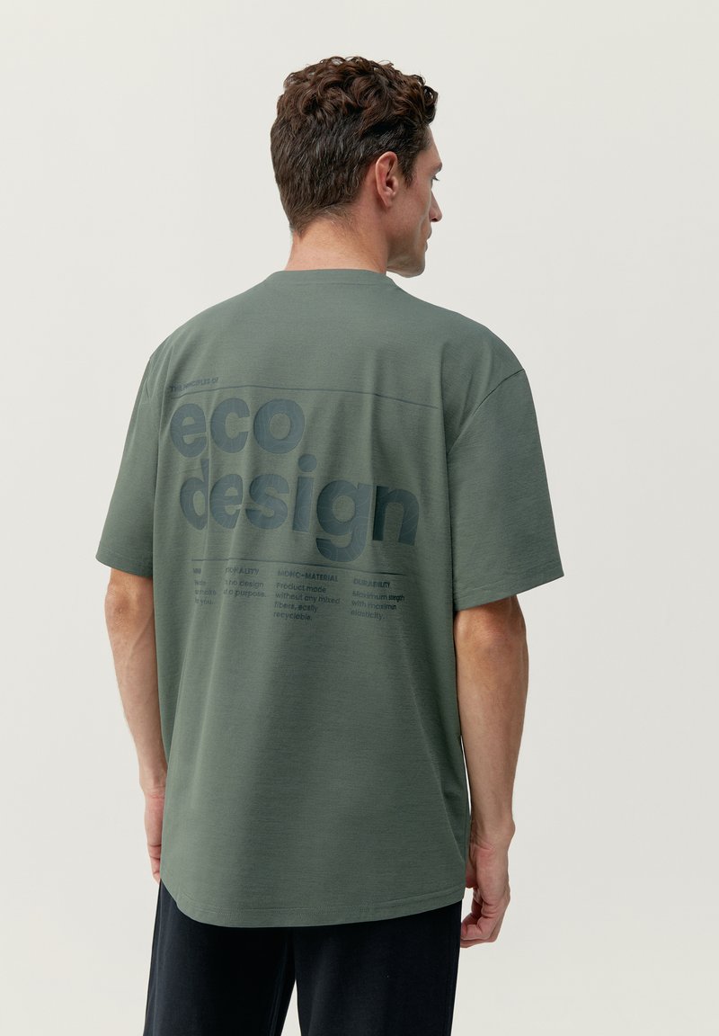 Zelené oversized tričko vyrobené z priedušnej látky, na chrbte s veľkým grafickým motívom "eko dizajn" a tmavým potlačou.