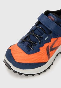 Buty sportowe z pomarańczową siateczką, granatowymi syntetycznymi wstawkami, czarnymi sznurówkami akcentującymi oraz ruggedną czarną podeszwą zapewniającą przyczepność.