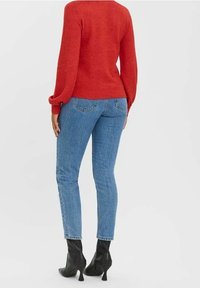 Roter Strickpullover mit Ballonärmeln, kombiniert mit hellblauen skinny Jeans und schwarzen, hohen Stiefeletten. Schlichtes Design und taillierte Silhouette.