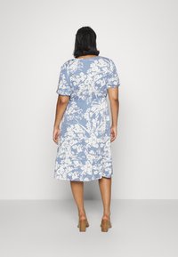 Vestido midi floral en azul claro con estampados blancos, mangas cortas, cintura ceñida y falda fluida. Tejido de algodón suave. Tacones gruesos.