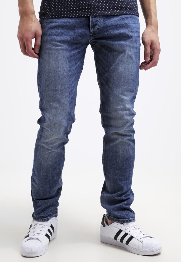 Slim-fit blå denimjeans med ljusblekningar och kontrasterande sömmar, i kombination med vita sneakers med svarta ränder.