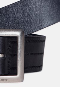 Cinturón de cuero negro con un acabado texturizado. Presenta una hebilla de metal plateado en forma de cuadrado y detalles de costura a lo largo de la correa.